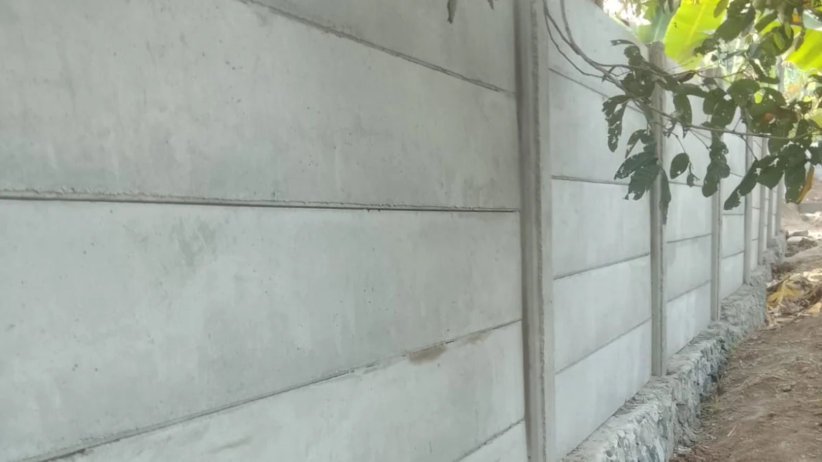 Deretan panel dan tiang pagar beton pracetak rapat di atas pondasi batu kali